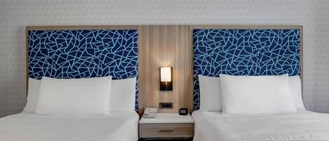 A hotel room with two beds, a nightstand with a lamp, and a wooden headboard.