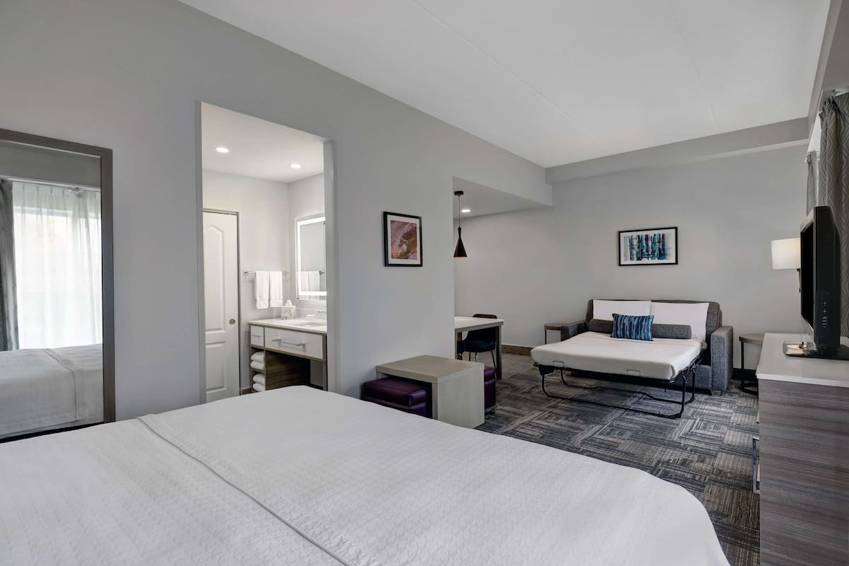 Ein modernes Hotelzimmer mit einem großen Bett, einer Schlafcouch, einem Schreibtisch und einem Fernseher.