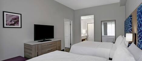 Une chambre d’hôtel avec deux lits, un téléviseur à écran plat, un ventilateur de plafond et un tableau encadré au mur.