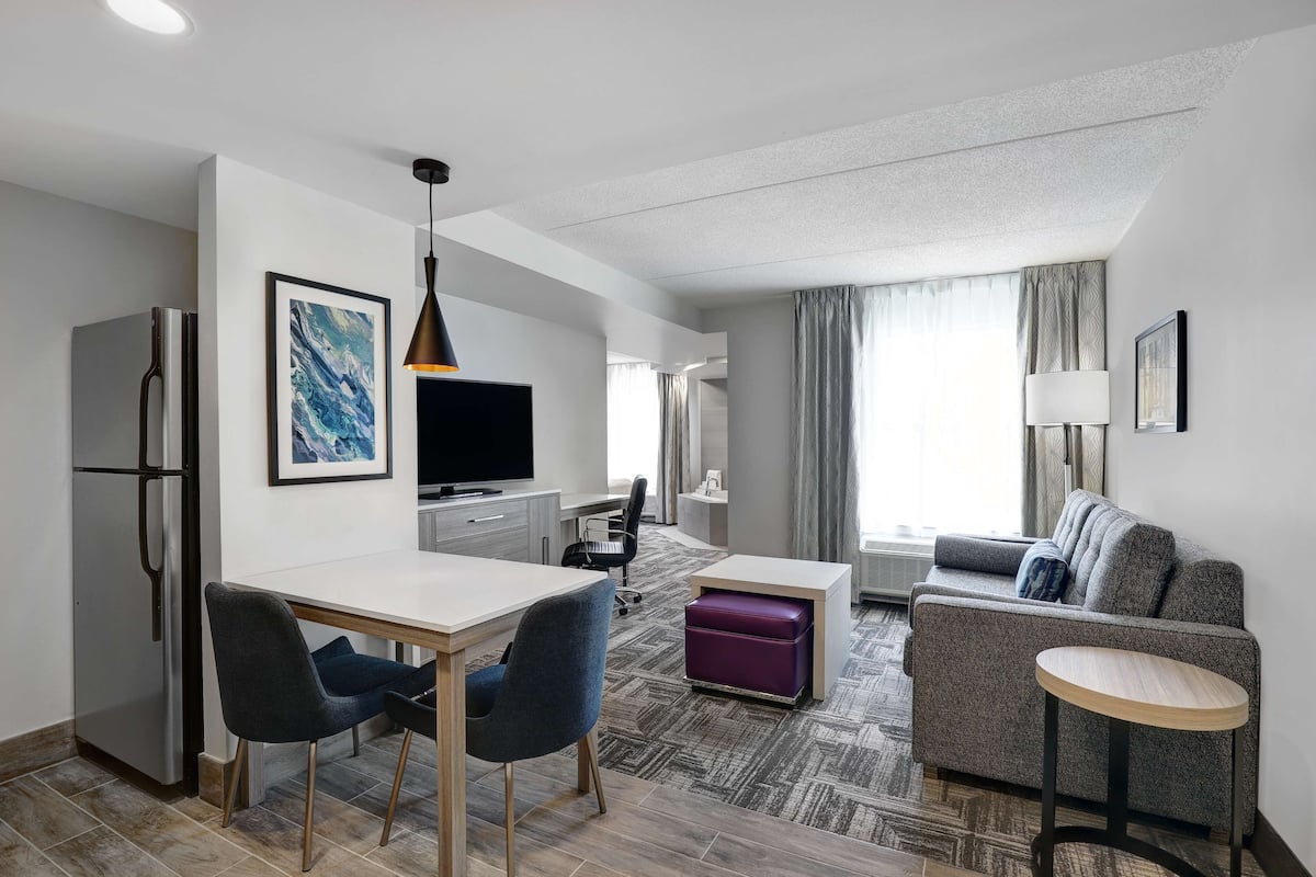 Ein modernes Hotelzimmer mit Essbereich, einer Couch, einem kleinen Tisch und einem Fernseher.