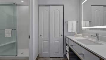 A modern bathroom with a glass shower enclosure, a white vanity with a large mirror, and a tiled floor.