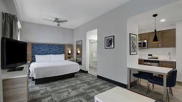 A hotel room with a bed, a desk, a TV, a ceiling fan, and a kitchenette.