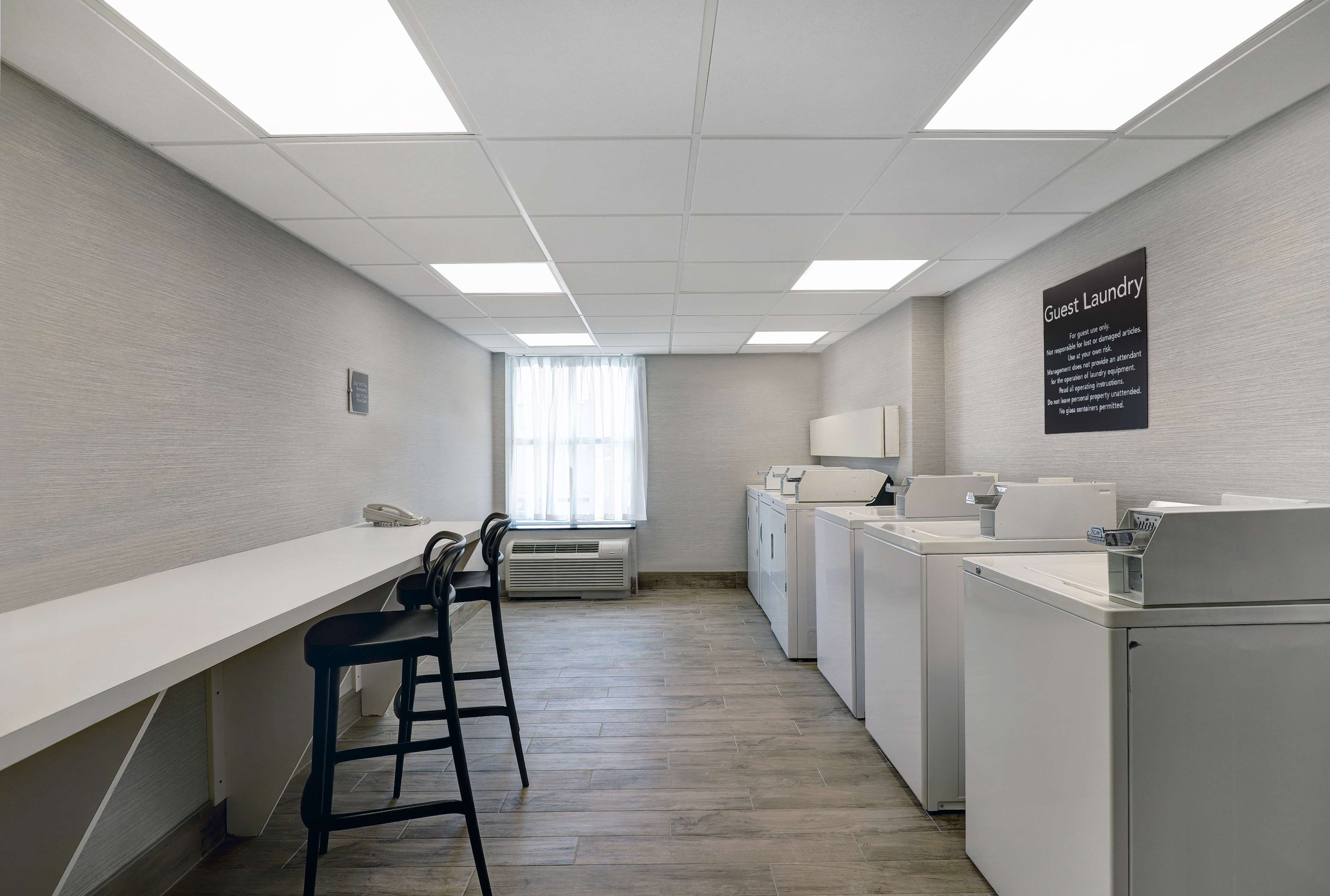 A laundry area with a sign indicating guest laundry services, a long counter, a telephone, and a chair.