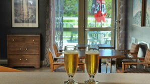 Deux verres de bière sur le comptoir d’un bar, avec en arrière-plan une vue sur les tables en plein air et un buffet en bois.