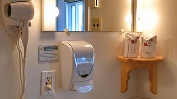 Une salle de bain équipée d’un sèche-cheveux, d’un sèche-mains, d’un miroir avec éclairage, d’un lavabo et d’un panier contenant des articles de toilette.