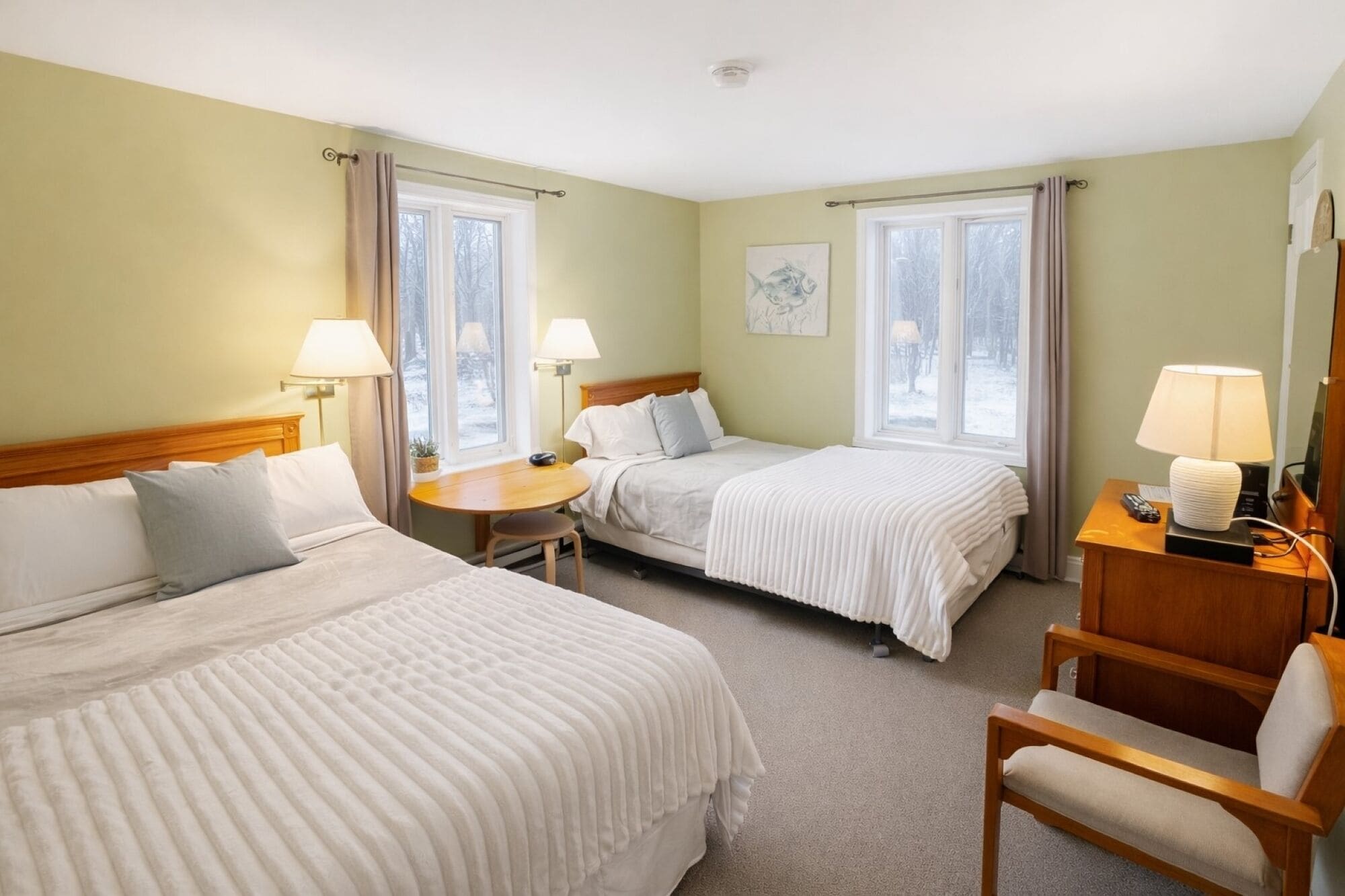 A hotel room with two beds, a small table, a chair, and a desk with a lamp.