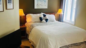 A hotel room with a bed, two bedside lamps, a flat-screen TV, a framed picture on the wall, and a window with curtains.