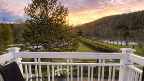 Une terrasse avec deux chaises et une petite table, offrant une vue panoramique sur un paysage verdoyant, avec des arbres et une étendue d’eau.