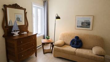 A room with a wooden dresser, a beige sofa, a floor lamp, and framed pictures on the walls.