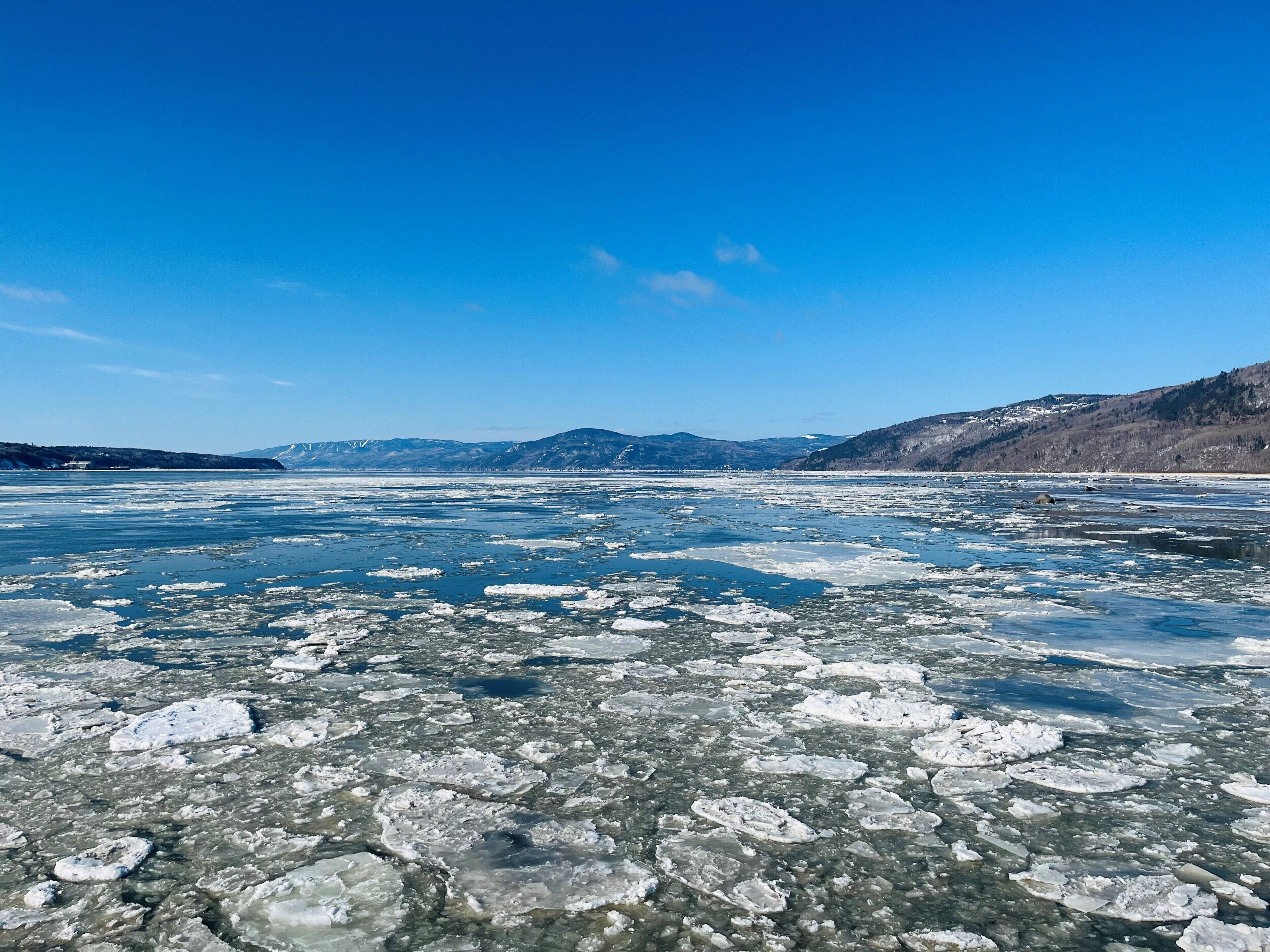 A frozen lake with clear ice and snow-covered hills in the background.