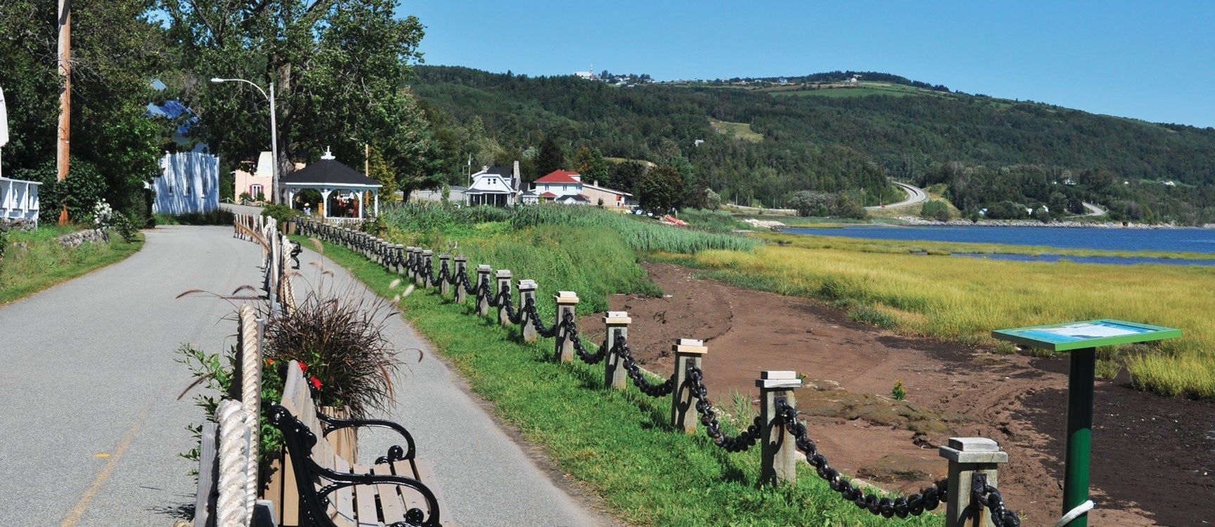 A paved road with a bicycle parked on the side, a chain-link fence, and a view of a lake and hills in the background.