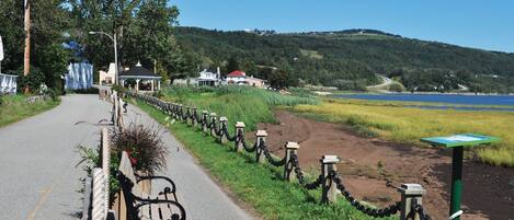 A paved road with a bicycle parked on the side, a chain-link fence, and a view of a lake and hills in the background.