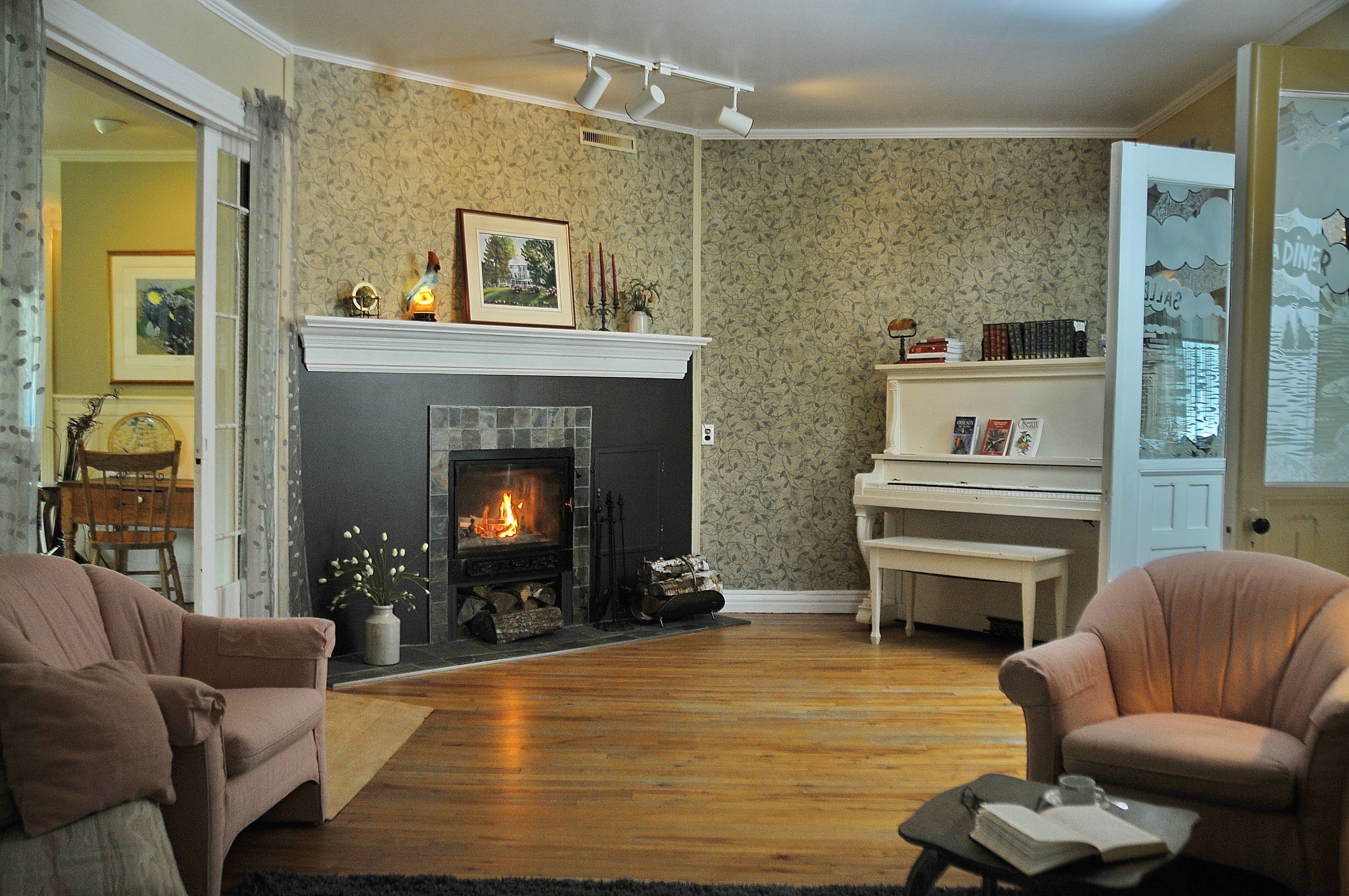 A cozy living room with a fireplace, two armchairs, a piano, and a bookshelf.