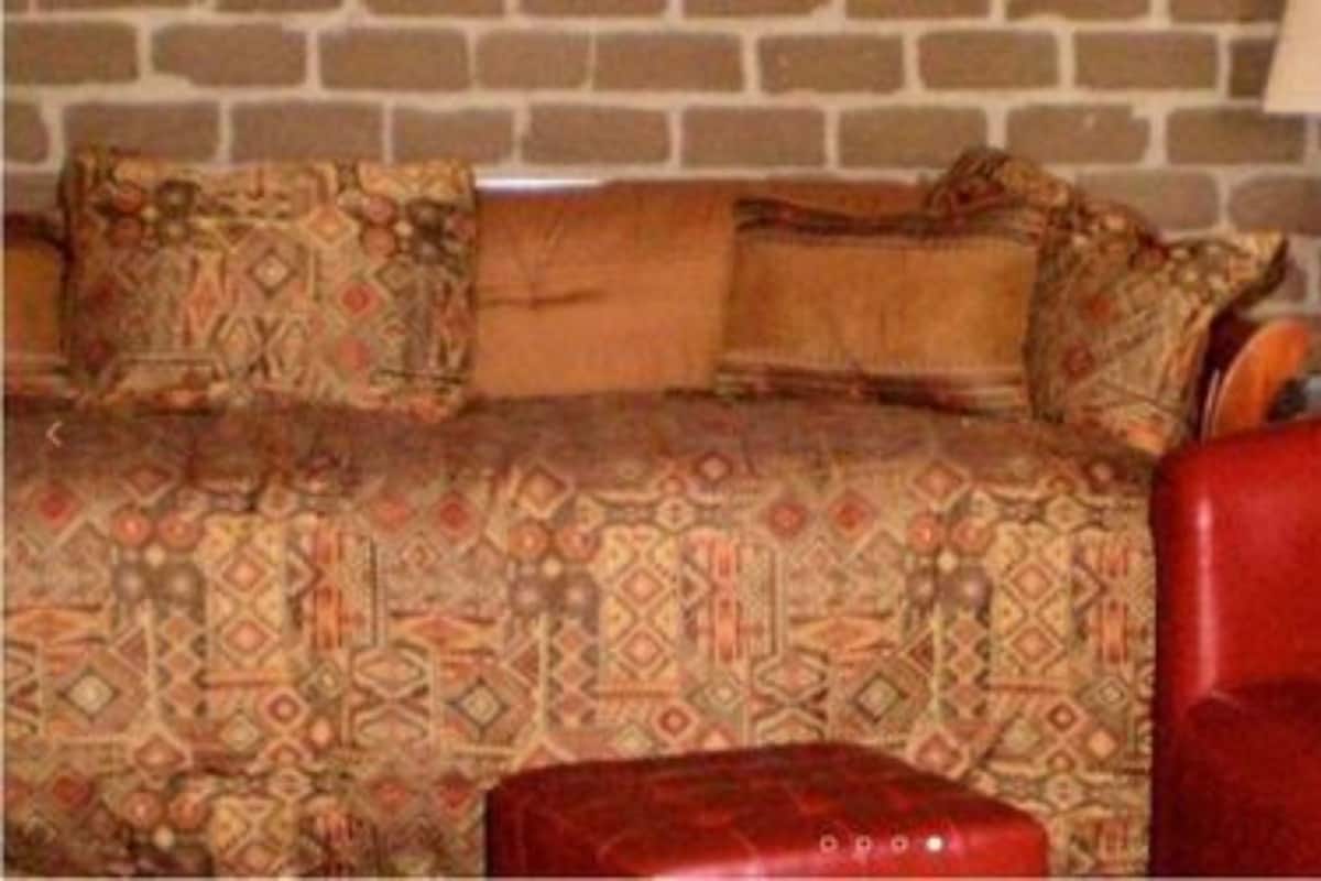 A room with a patterned sofa set, a red armchair, and a lamp against a brick wall.