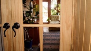 Une porte en bois donnant sur une pièce où l’on aperçoit une chaise, une plante en pot et un seau bleu.