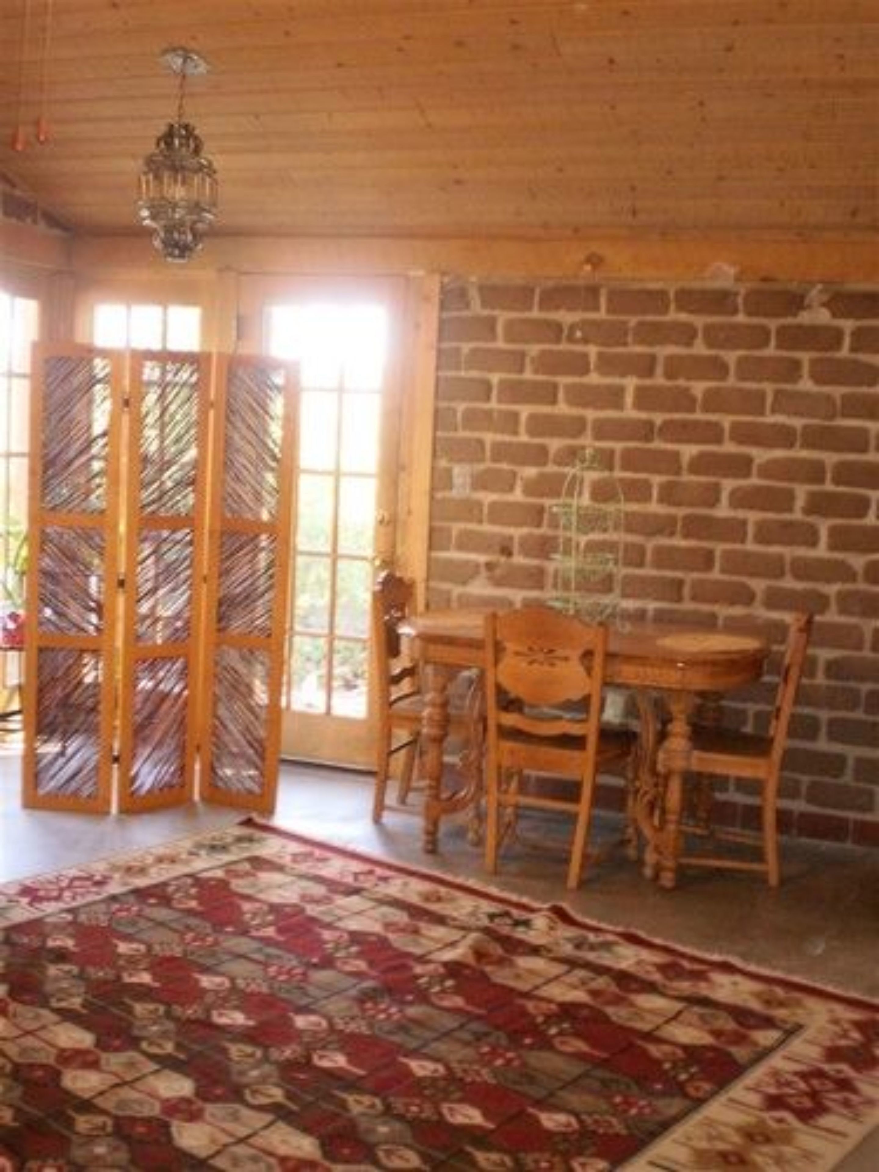 A room with a wooden table and chairs, a patterned rug, and a brick wall.
