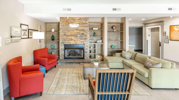 A modern living room with a stone fireplace, red and green sofas, and a wooden coffee table. - Country Inn & Suites by Radisson, Smyrna - Atlanta Northwest (Smyrna)