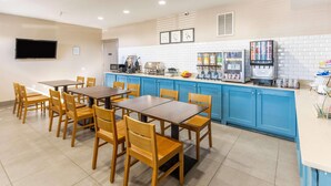 A hotel dining area with wooden tables and chairs, a kitchen counter with appliances, and a tiled floor. - Country Inn & Suites by Radisson, Smyrna - Atlanta Northwest (Smyrna)