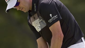 A golfer in a black shirt and white pants, holding a golf club.