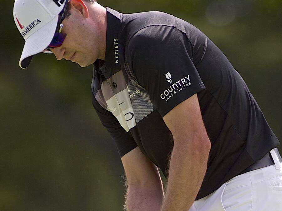 A golfer in a black shirt and white pants, holding a golf club.