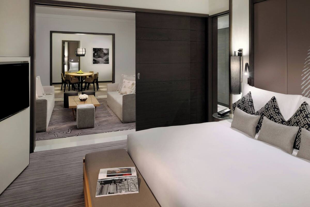 A modern hotel room with a large bed, a sofa, a dining area, and a TV.