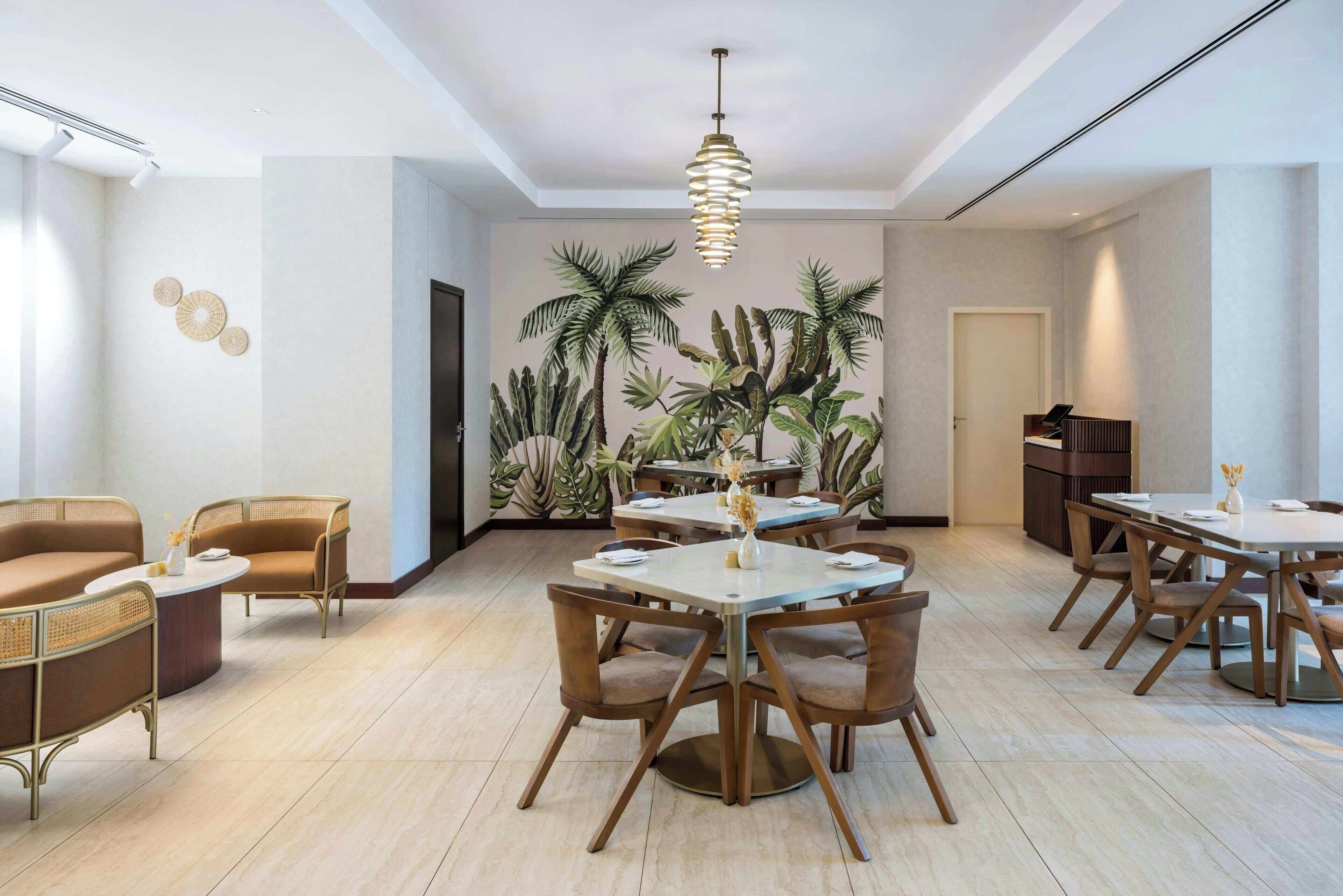 A modern dining area with round tables and chairs, a hanging light fixture, and a wall mural of tropical plants.