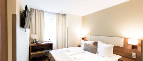 Une chambre d’hôtel avec un grand lit, des tables de chevet, un bureau avec une lampe, une télévision et une fenêtre avec des rideaux.