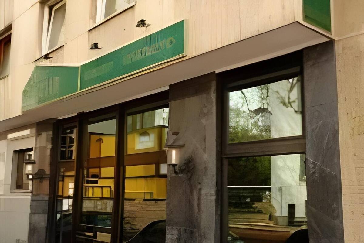 Ein Gebäude mit einem grünen Schild über dem Eingang, großen Fenstern und einem sichtbaren Innenraum mit gelben Wänden und einer Treppe.