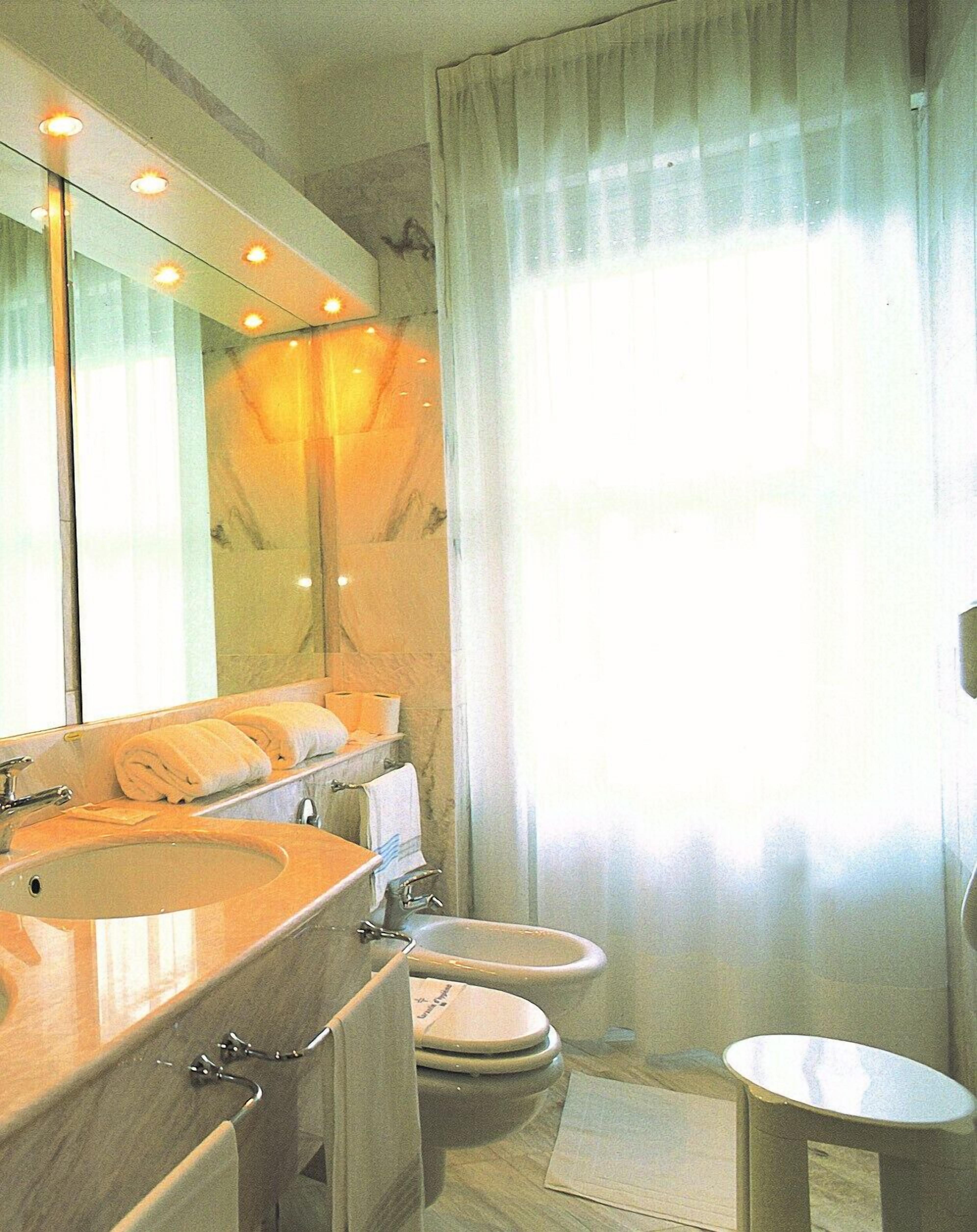 Une salle de bain avec un grand miroir, un lavabo, deux toilettes et un rideau de douche.