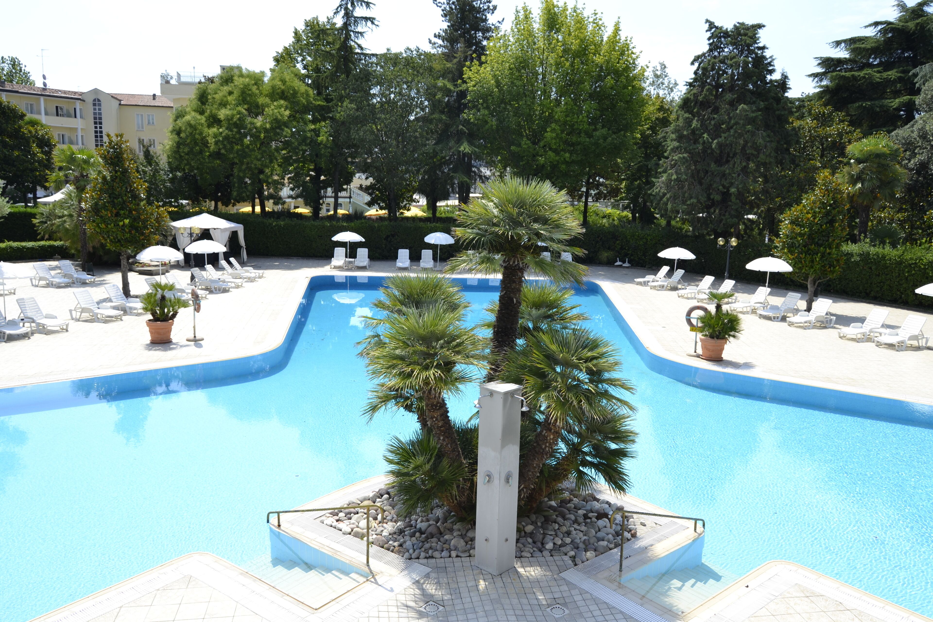 Une piscine entourée d’arbres et de plantes en pot, avec des chaises longues et des parasols.