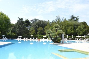 Une piscine entourée d’arbres, avec des chaises longues et des parasols.