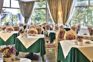 Un espace repas avec des tables dressées, des chaises aux motifs décoratifs et une vue sur la verdure environnante.