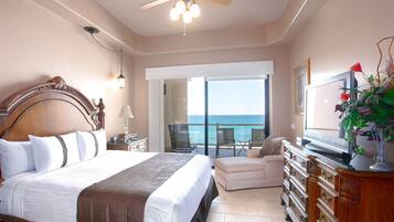 A bedroom with a large bed, a ceiling fan, a TV, and a view of the ocean.