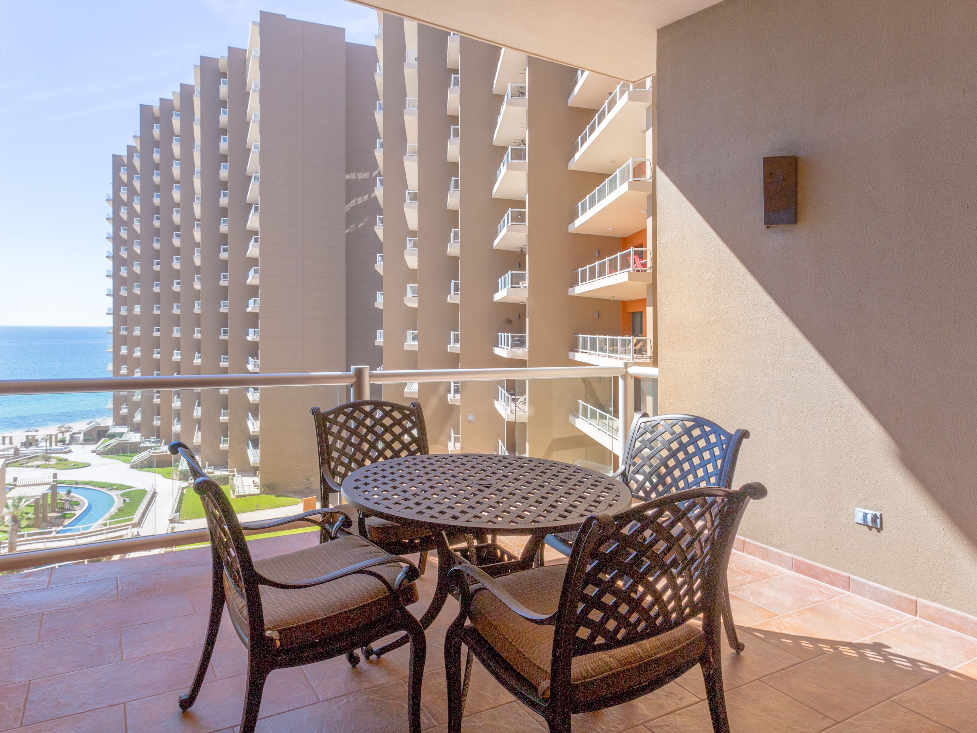 A balcony with a round table and chairs, overlooking a high-rise building and a view of the ocean.