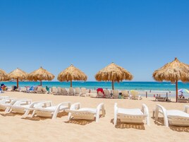 A beach with rows of white lounge chairs and thatched umbrellas.