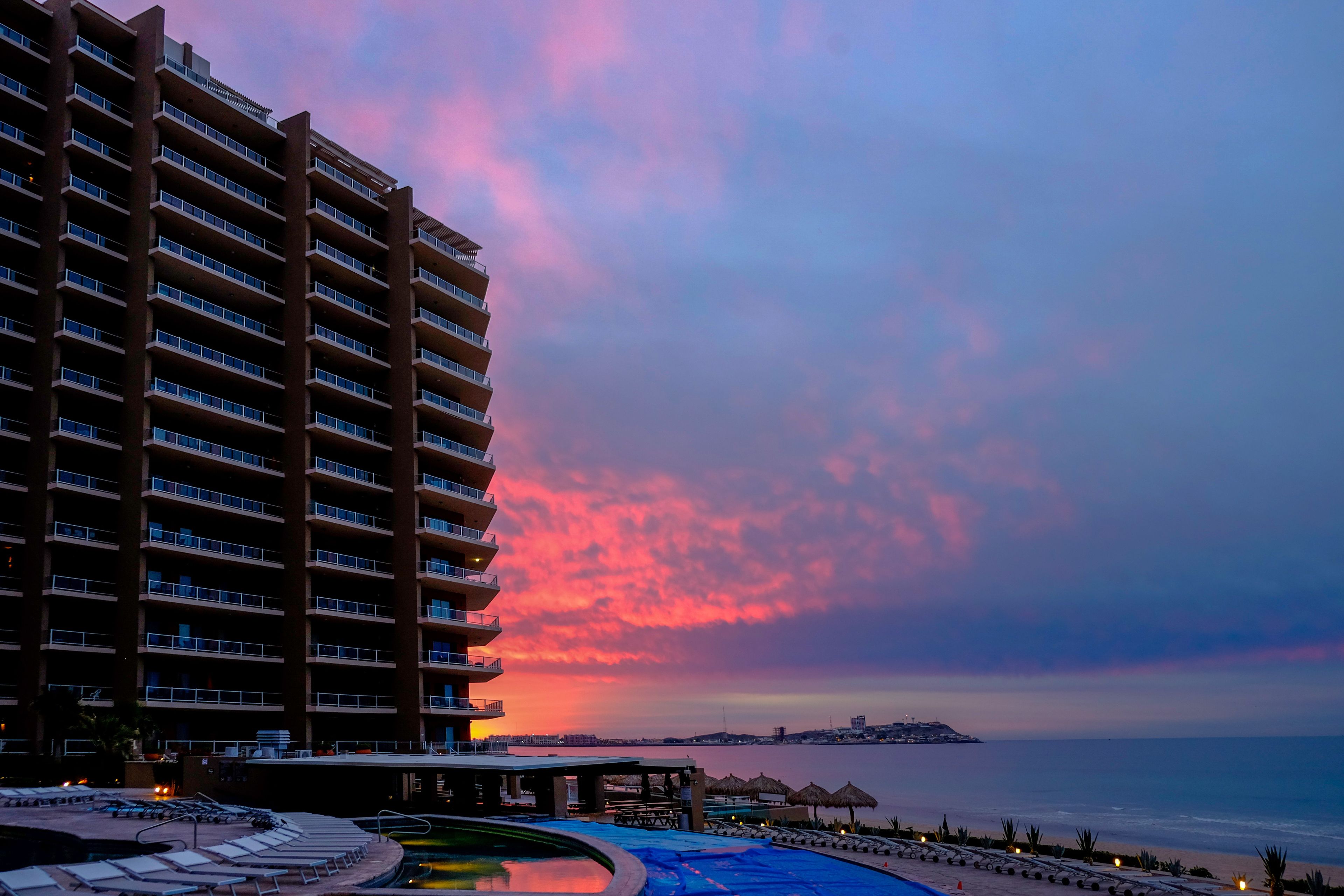 Un hotel de gran altura con zona de piscina y vista al mar al atardecer.