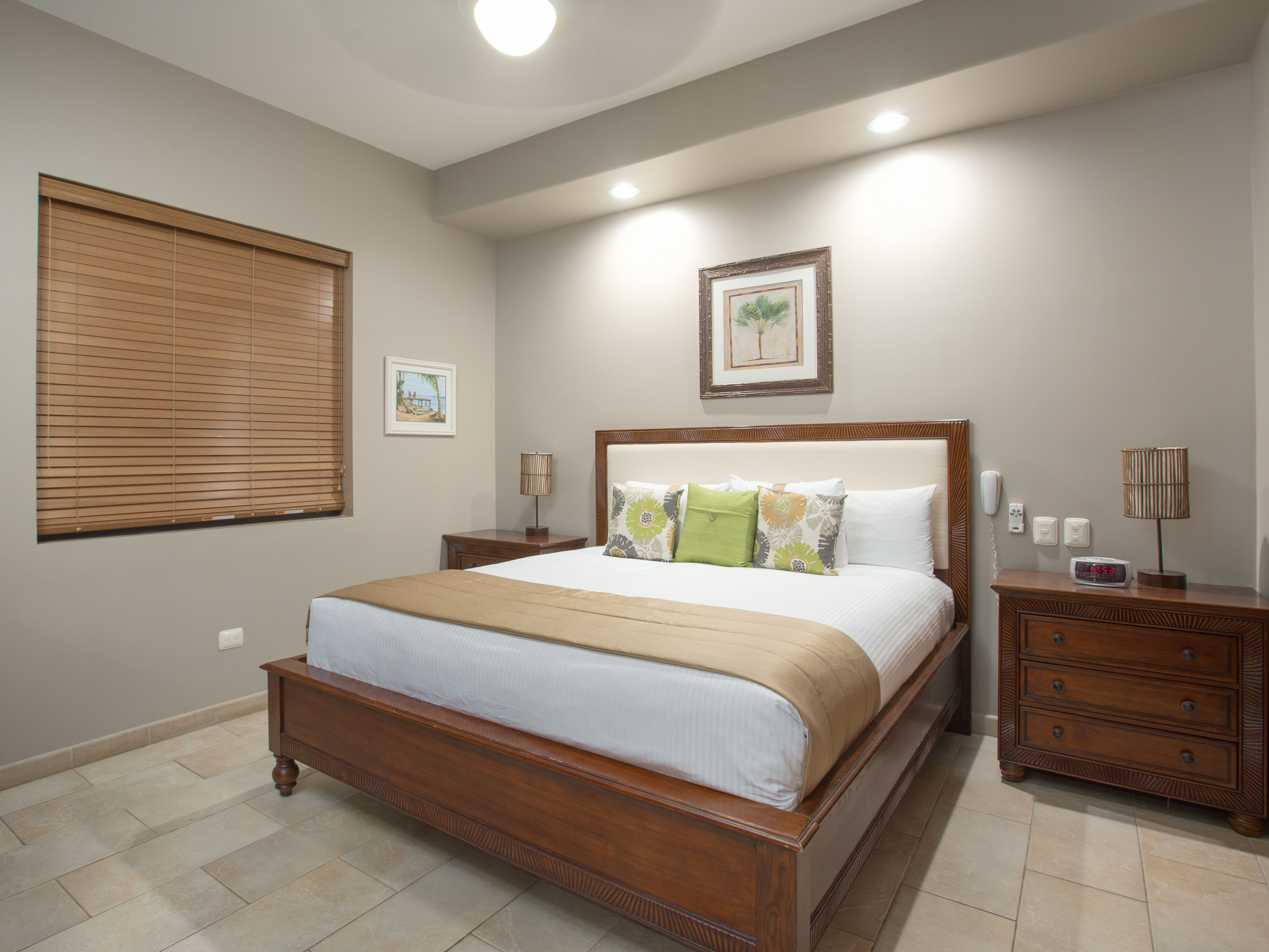 A bedroom with a wooden bed, a nightstand, a bedside table, a wall clock, and two framed pictures.