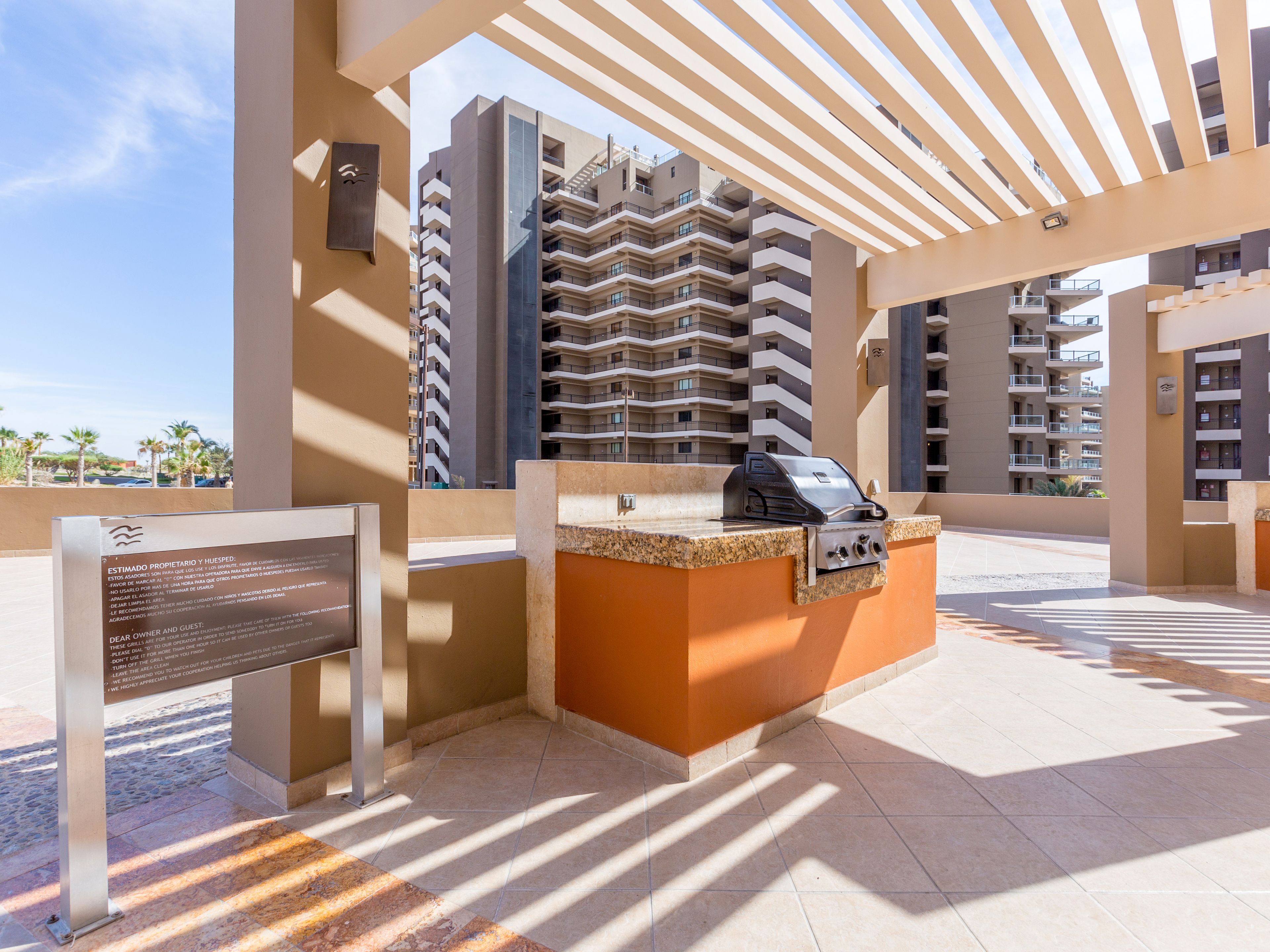 Un patio en la azotea con una parrilla, un letrero y vistas de edificios altos.