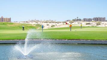 Golfers tee off amidst a serene water feature and well-manicured green.