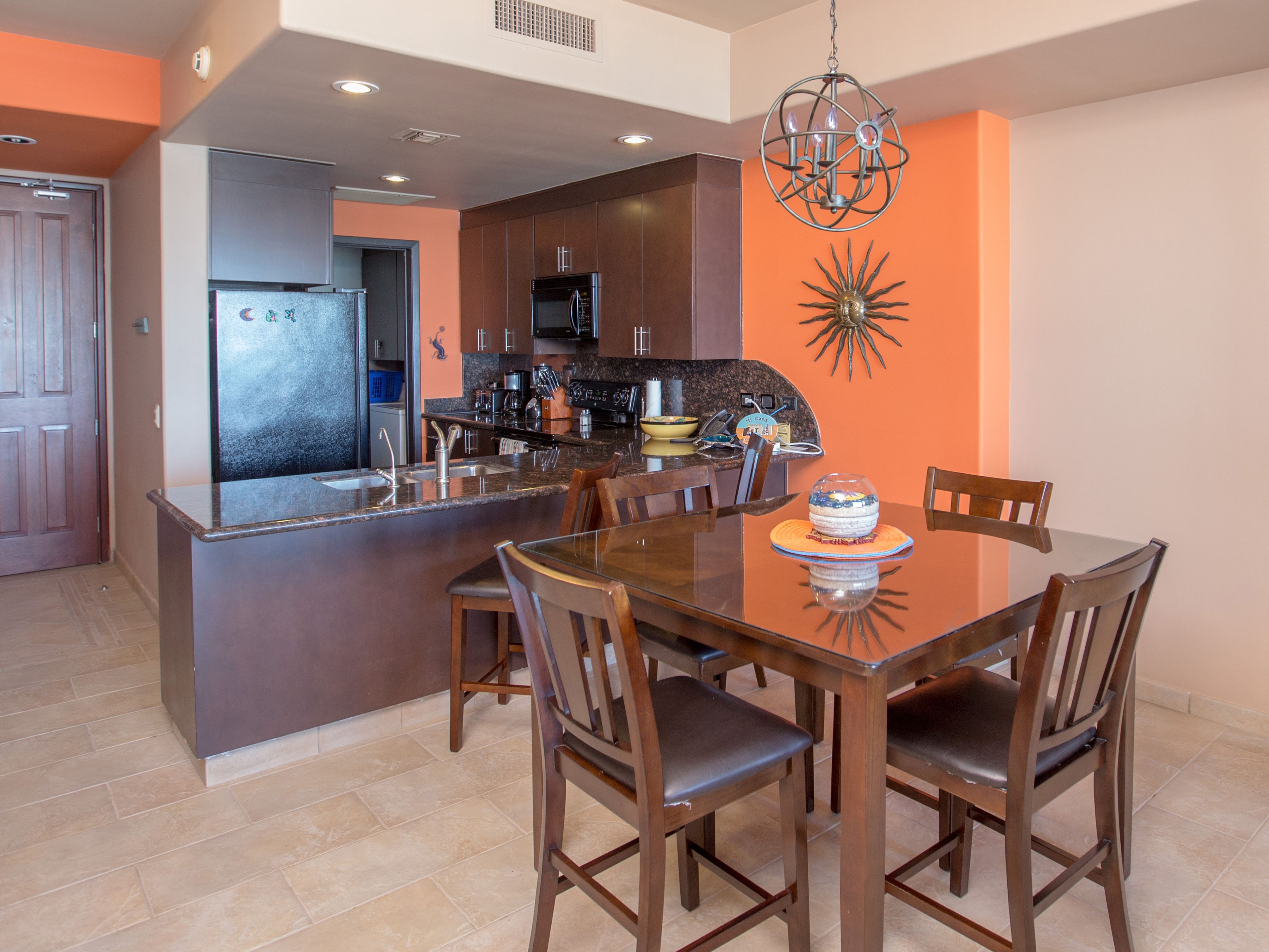 A modern kitchen with dark cabinetry, a central island, and a dining area with wooden chairs and a glass table.