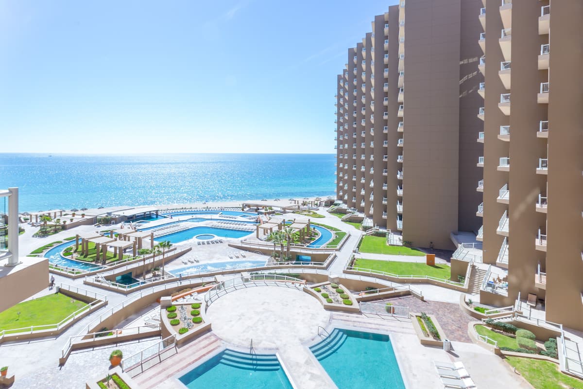 Un resort con varias piscinas, una piscina circular central y vista al océano.