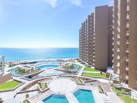 A resort with multiple swimming pools, a central circular pool, and a view of the ocean.