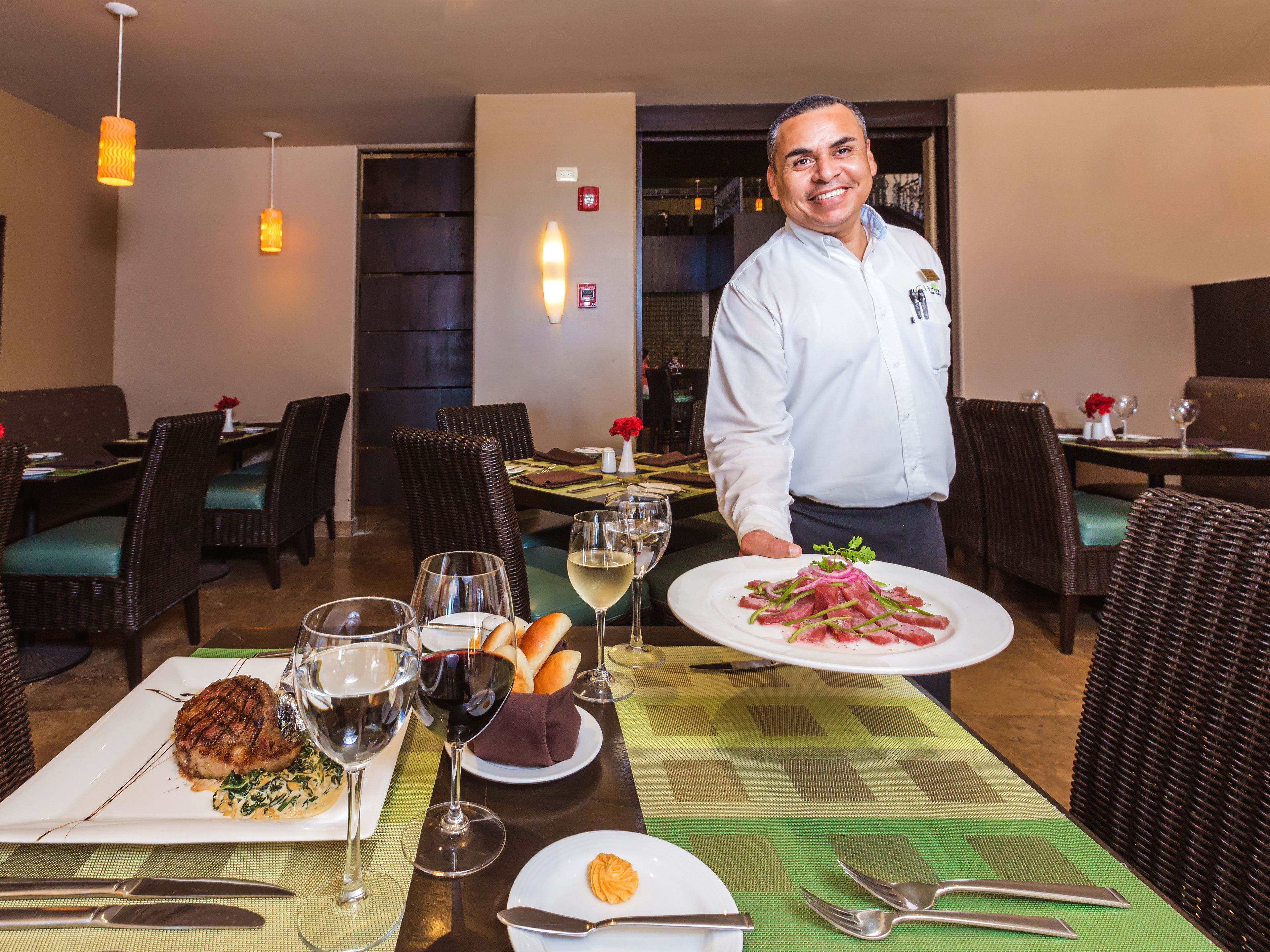 Interno di un ristorante con tavoli, sedie e un cameriere che porta un piatto.