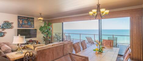A spacious dining area with a view of the ocean, featuring a large table, comfortable seating, and decorative elements like a starfish lamp and artwork.