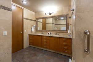 Un baño con un espejo grande, dos lavabos, armarios de madera y piso de baldosas.