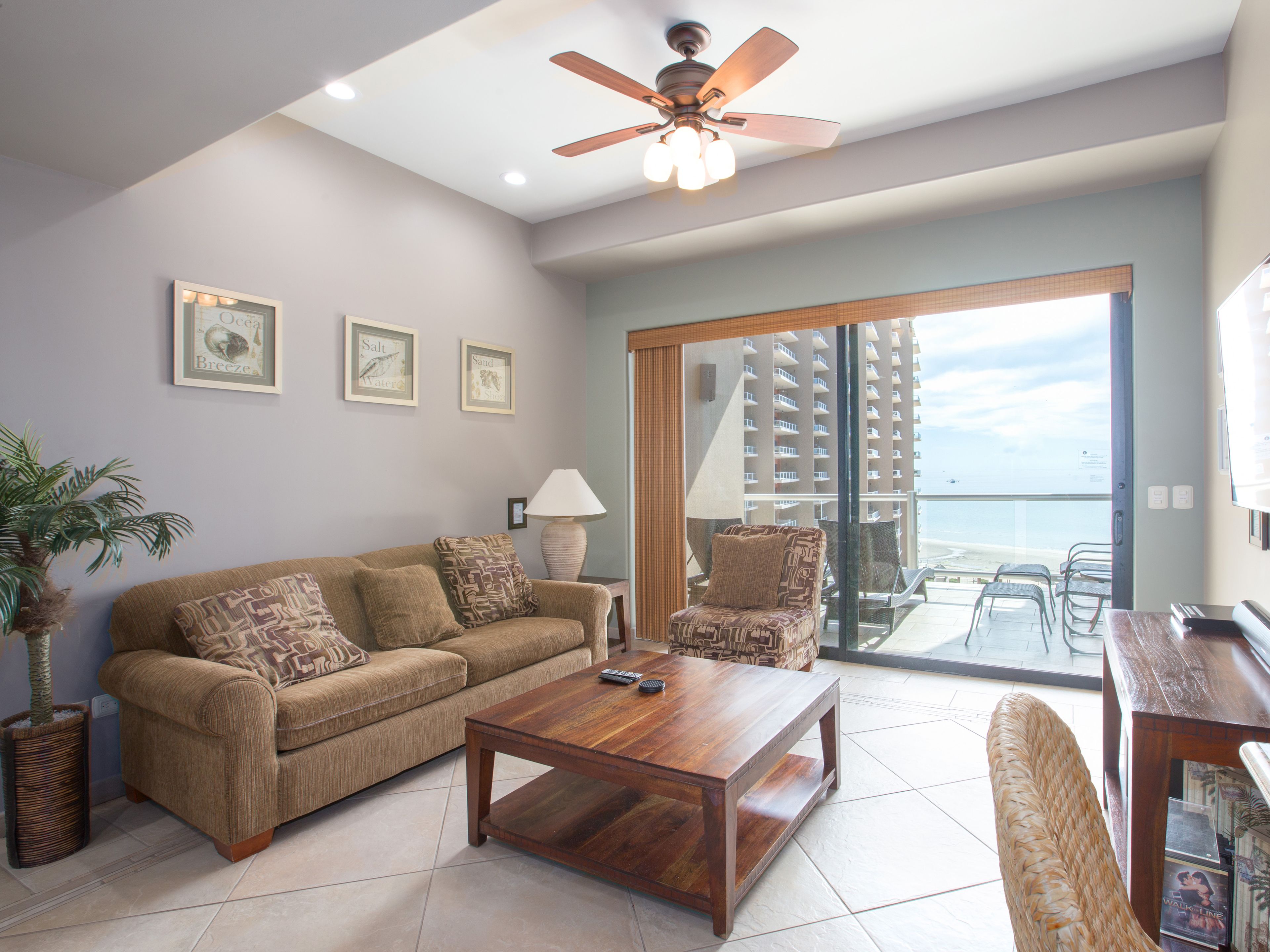 A living room with a sofa, coffee table, and chairs, a ceiling fan, and a view of a building through a glass door.
