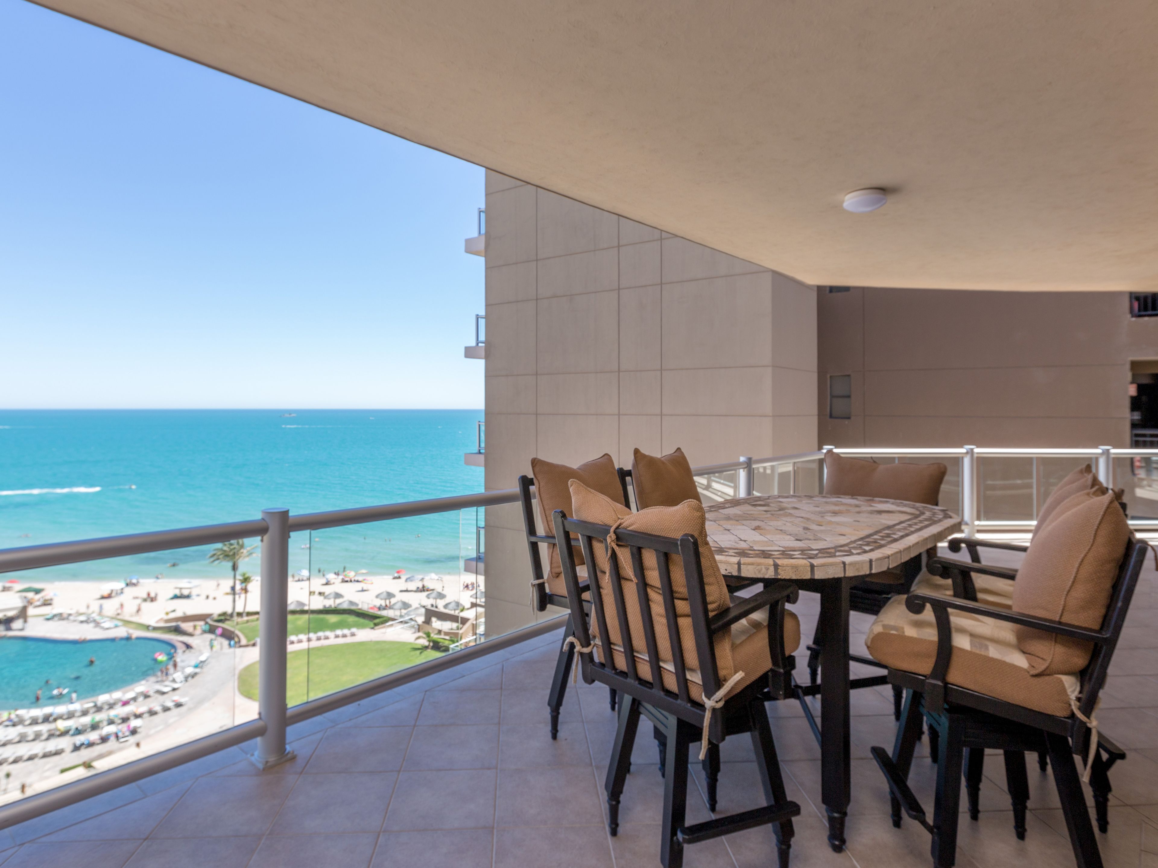 Un balcon avec une table et des chaises, donnant sur une plage et l’océan.