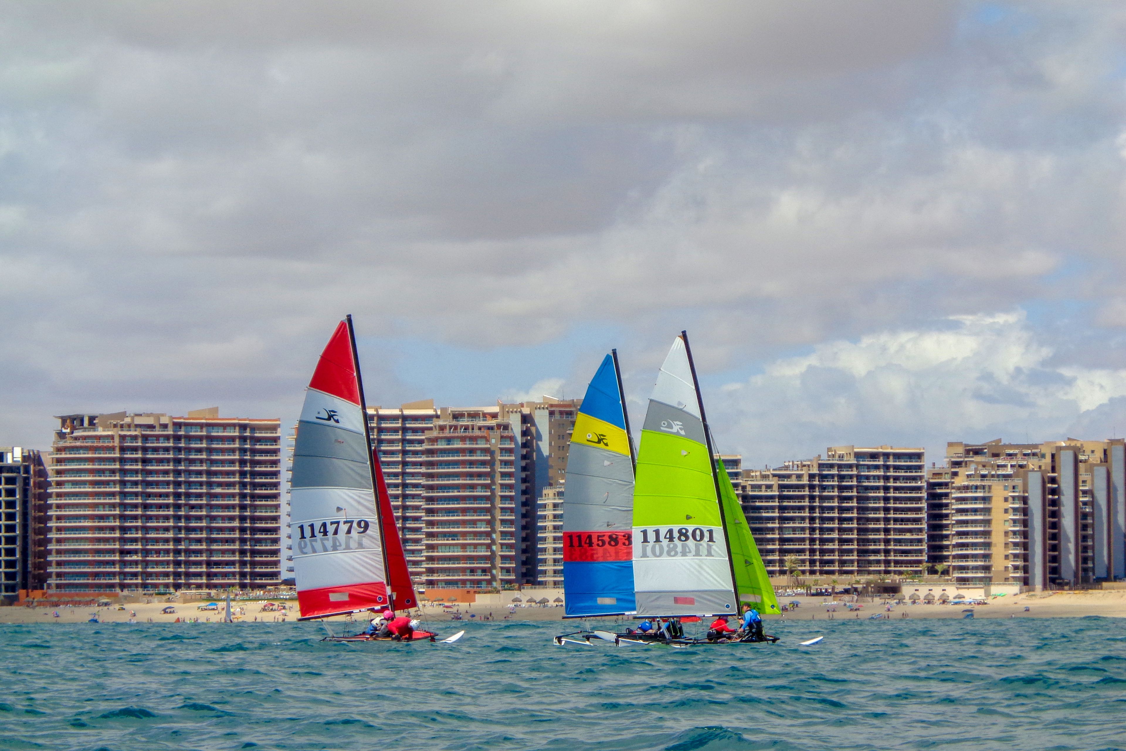 A beach with sailboats and a hotel in the background.