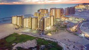 Un complejo hotelero frente al mar con varias torres altas, una playa y servicios bien iluminados.