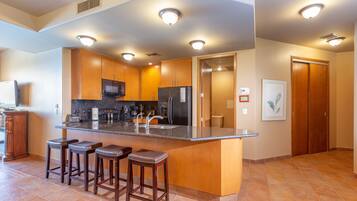 A modern kitchen with a central island, bar stools, wooden cabinets, and built-in appliances.